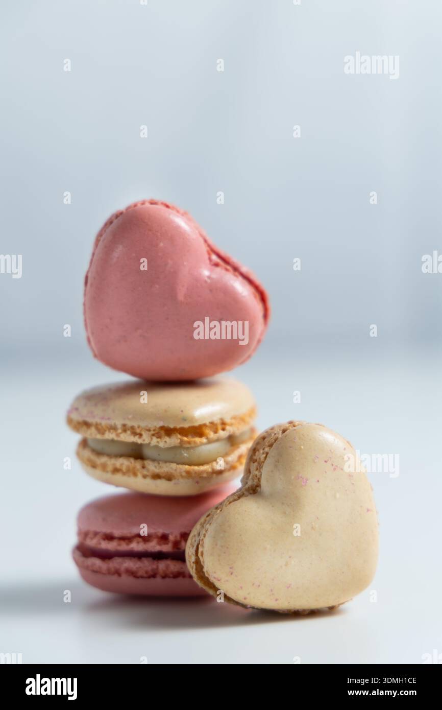 Tre macaron a forma di cuore sono disposti in una pila. Il macaron superiore è rosa, mentre quello al centro è di colore crema chiaro. Foto Stock