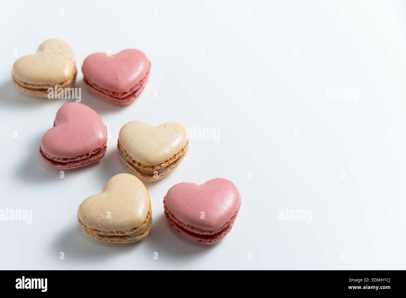Diversi biscotti a forma di cuori sono collocati su una superficie bianca pulita. I biscotti sono di due colori, rosa e beige. Foto Stock