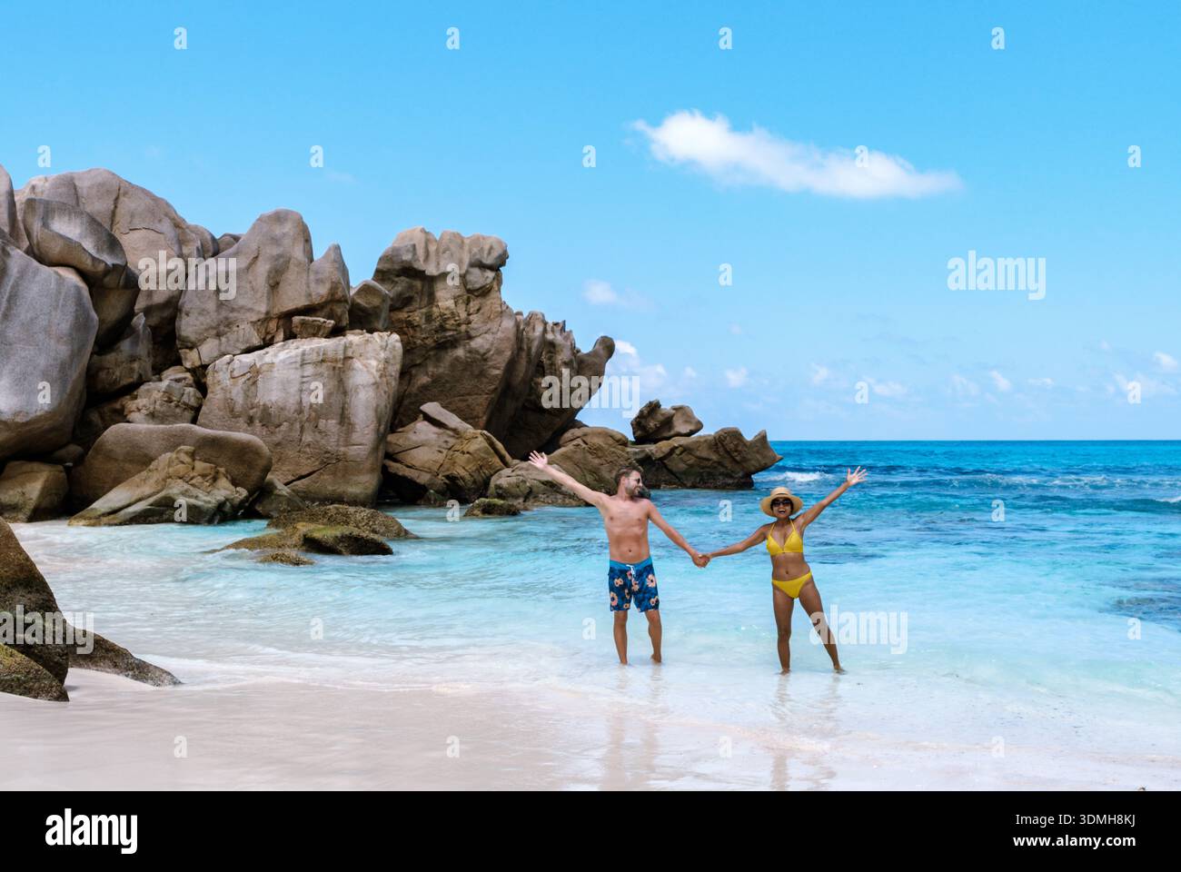 Trascorrendo una giornata di pace alla spiaggia di Anse Cocos, una coppia si trova mano nella mano nelle acque azzurre di la Digue Seychelles, circondati da splendidi graniti Foto Stock