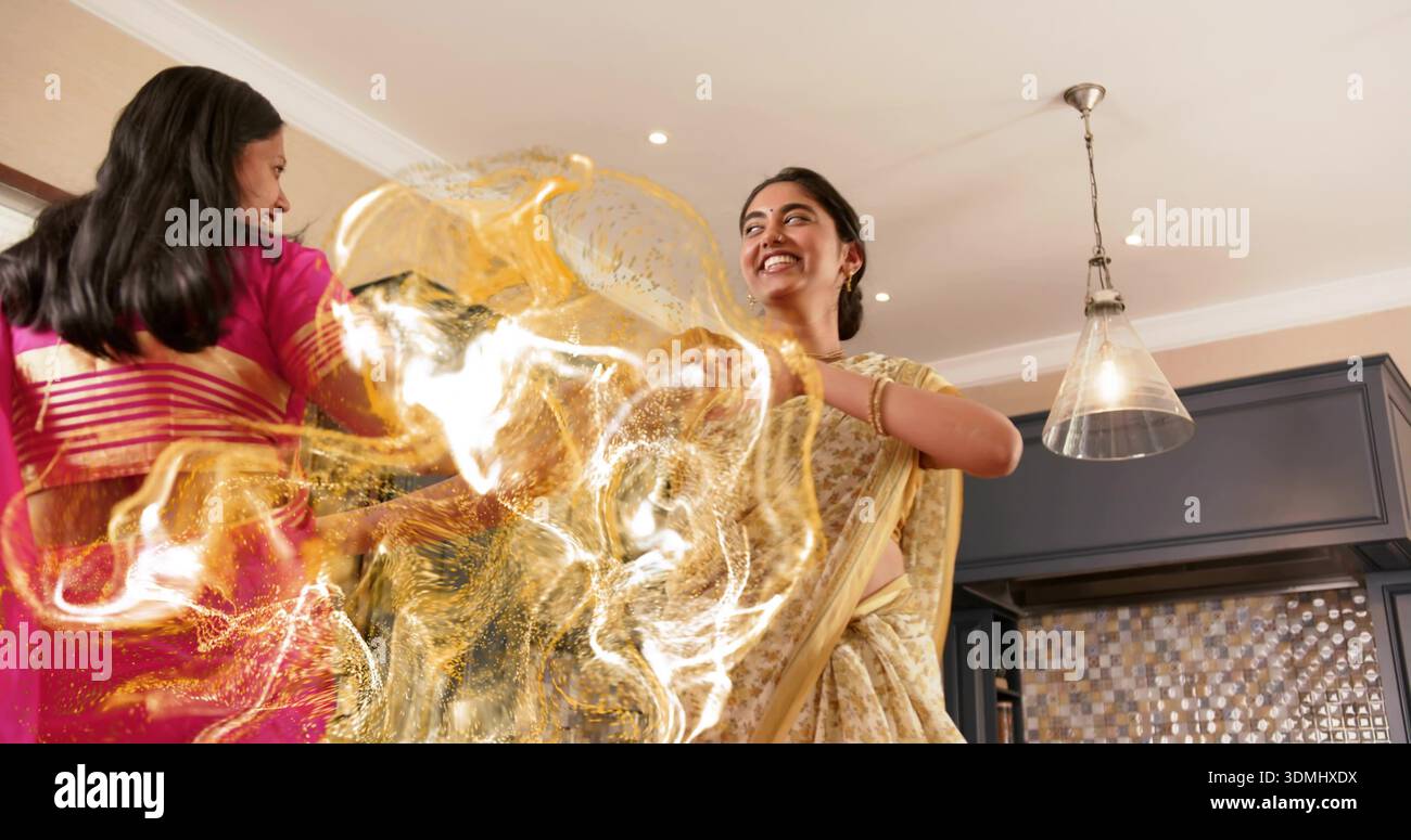 Donna danzante in oro giallo pallido sari che girano nella cucina di casa, con sari rosa, lampada a sospensione Foto Stock