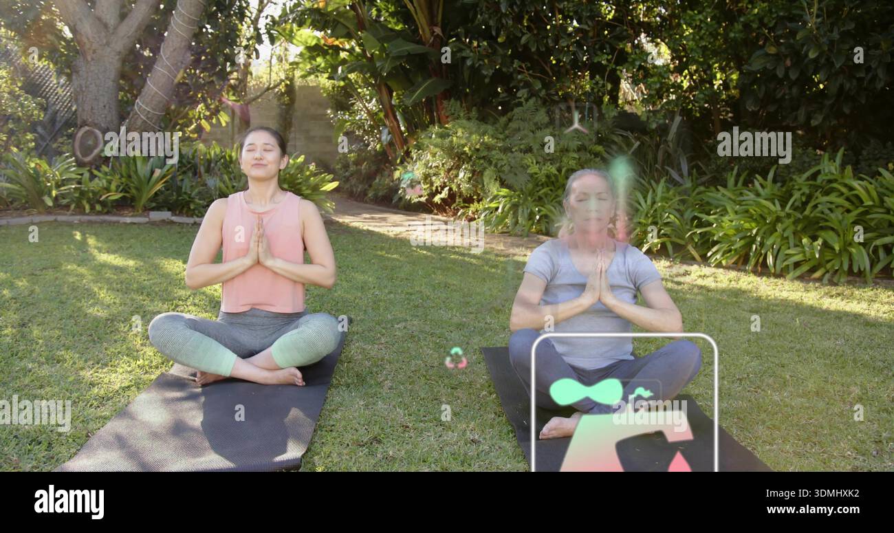 Meditare due donne sedute nel giardino sul retro con abiti da yoga su tappeti neri con rivestimento digitale Foto Stock