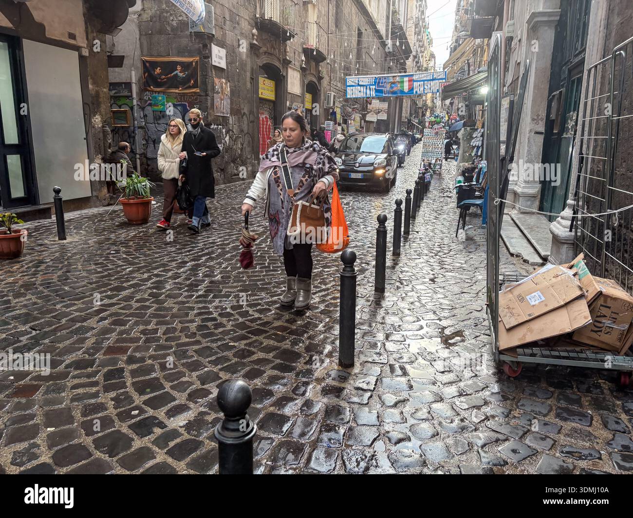 Strada acciottolata bagnata (sanpietrini) nell'affollato centro storico (Centro storico) di Napoli, Italia. Pedoni e traffico di veicoli in vicoli stretti Foto Stock