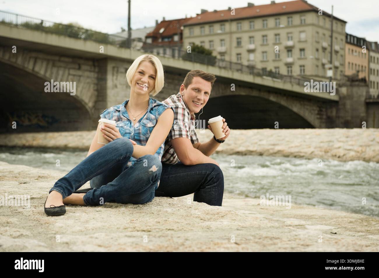 Giovane coppia seduta sul fiume a gustare un caffè insieme Foto Stock