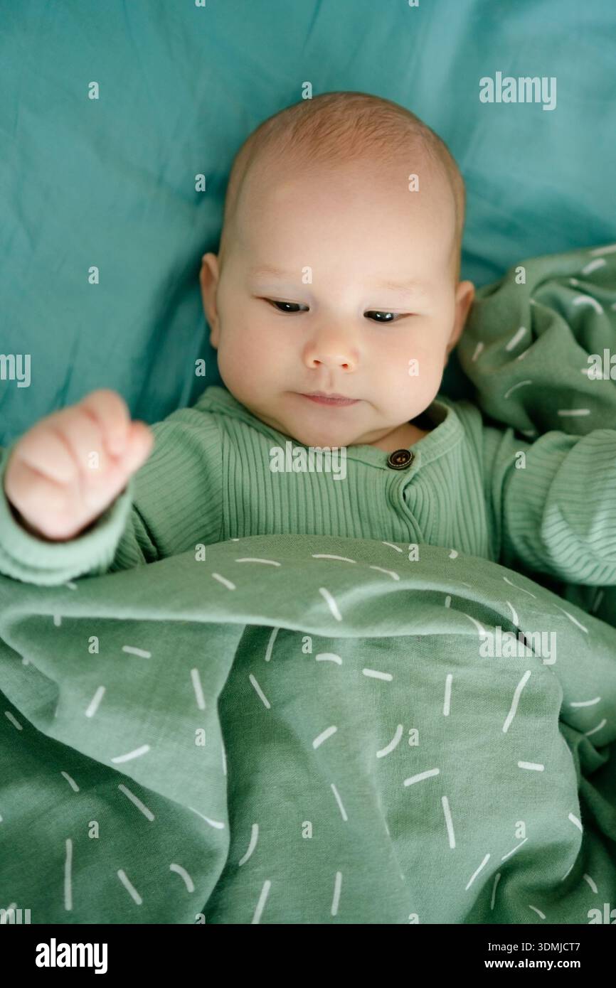 Un bambino giocoso si diverte avvolto in una coperta verde, mettendo in risalto il legame, la gioia e le pietre miliari dello sviluppo in un ambiente amorevole e nutriente. Foto Stock