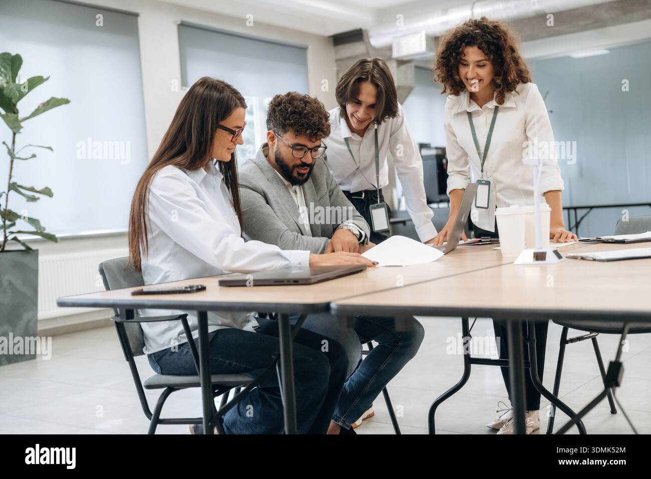 Seduti accanto al tavolo con il computer portatile. Un gruppo di persone lavora in ufficio insieme come un team. Foto Stock