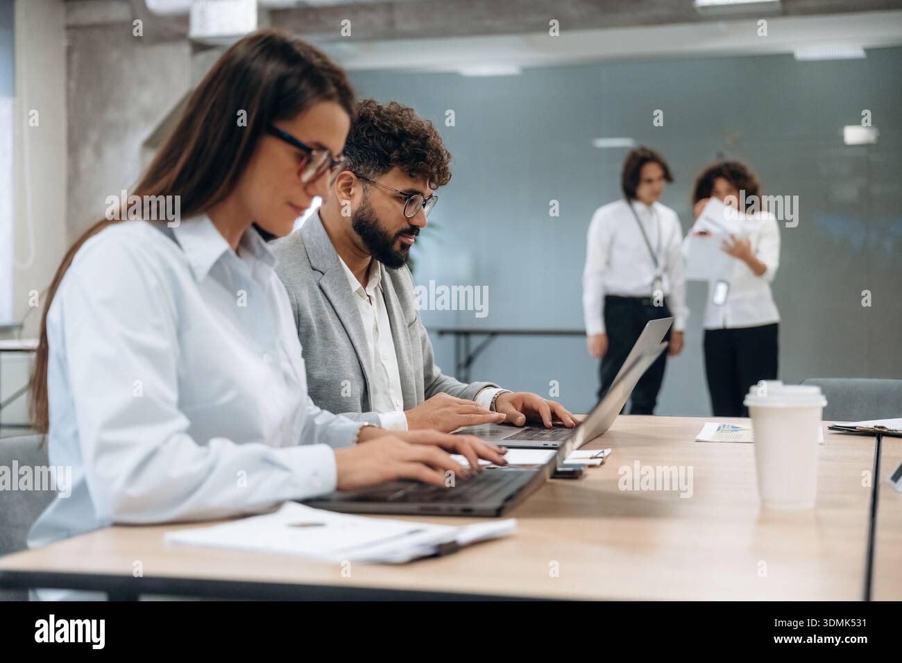 Seduti accanto al tavolo con il computer portatile. Un gruppo di persone lavora in ufficio insieme come un team. Foto Stock