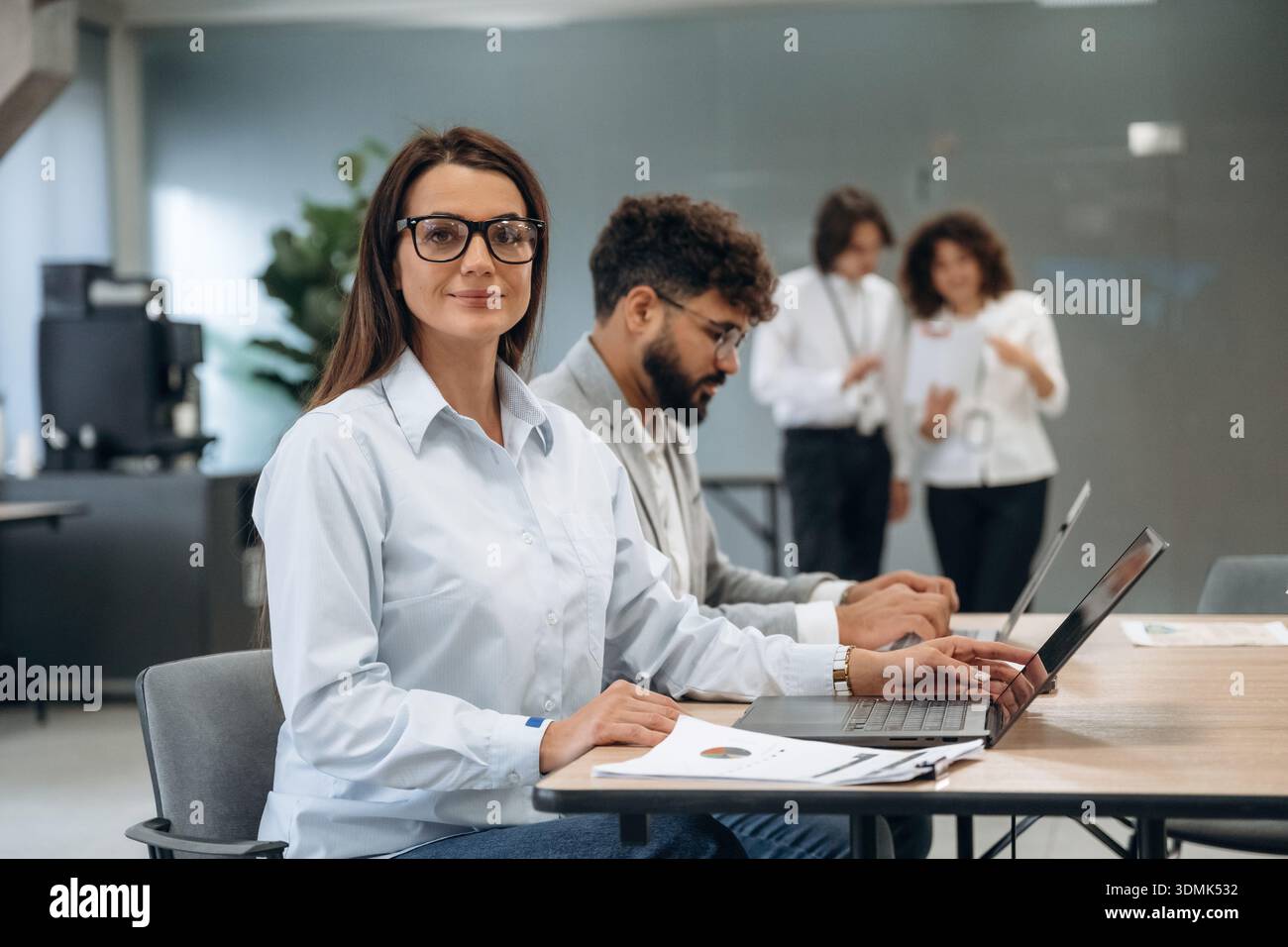 Seduti accanto al tavolo con il computer portatile. Un gruppo di persone lavora in ufficio insieme come un team. Foto Stock