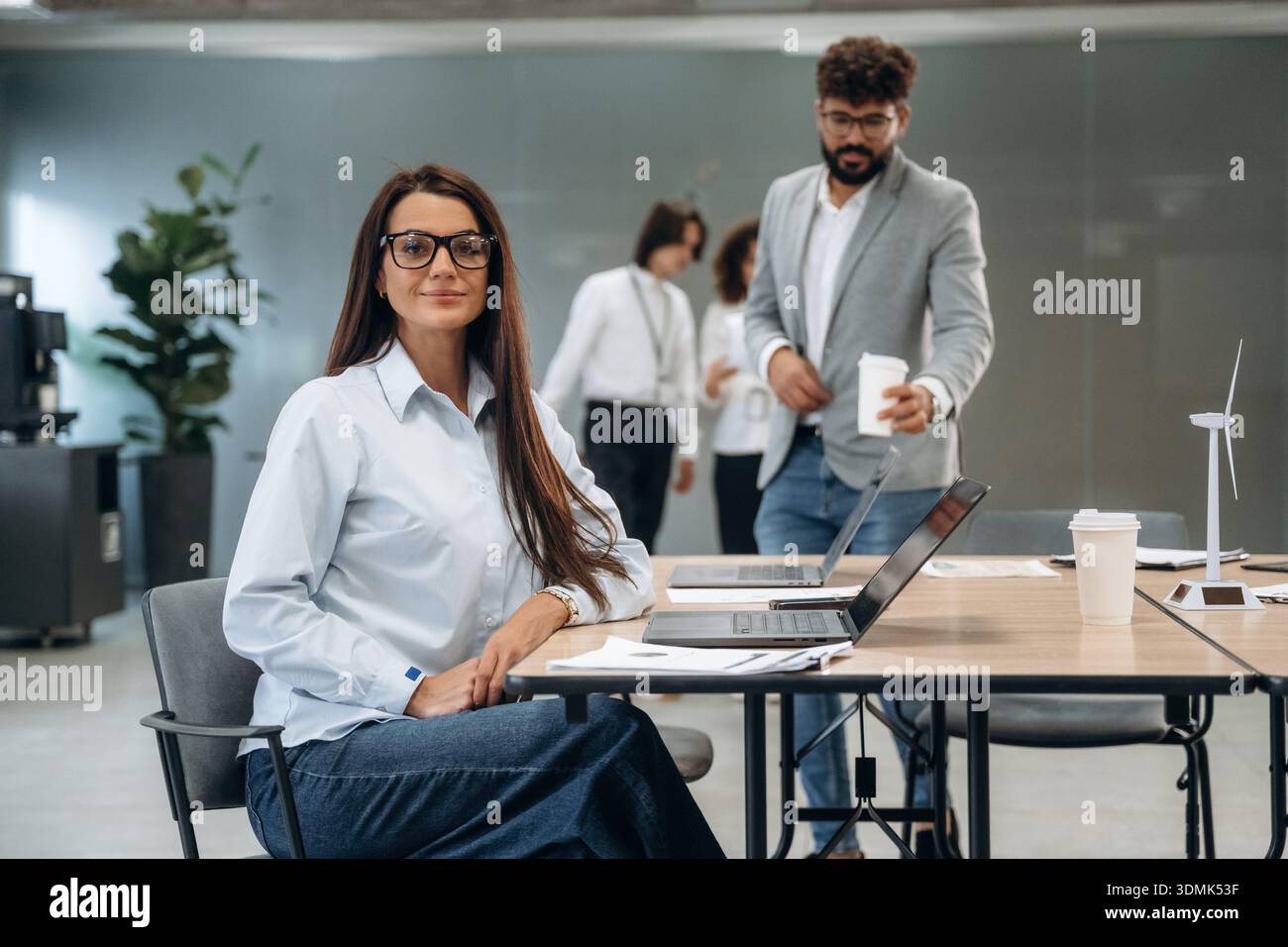 La donna è seduta e guarda la telecamera. Un gruppo di persone lavora in ufficio insieme come un team. Foto Stock