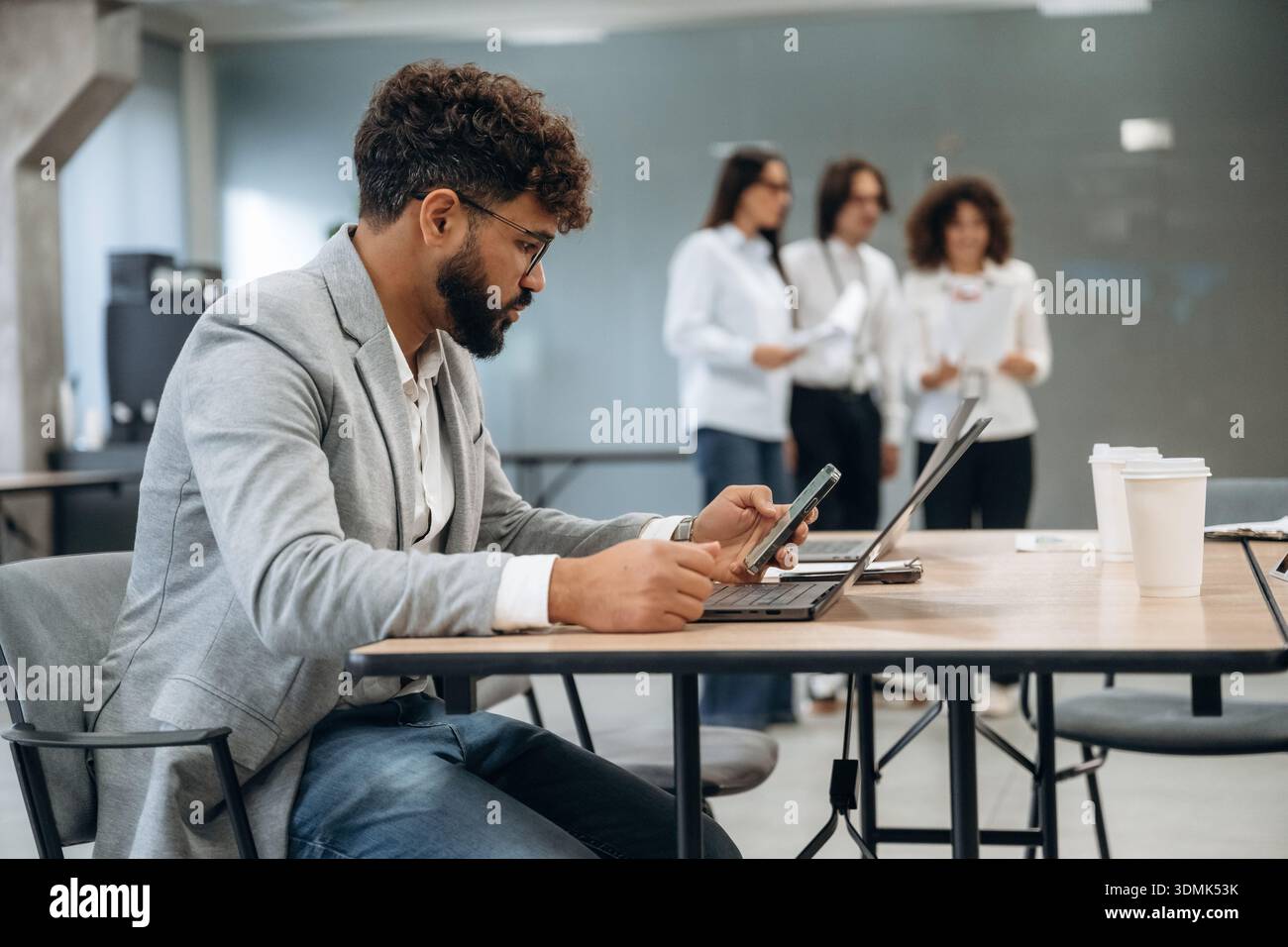 L'uomo con gli occhiali è seduto sulla sedia. Un gruppo di persone lavora in ufficio insieme come un team. Foto Stock