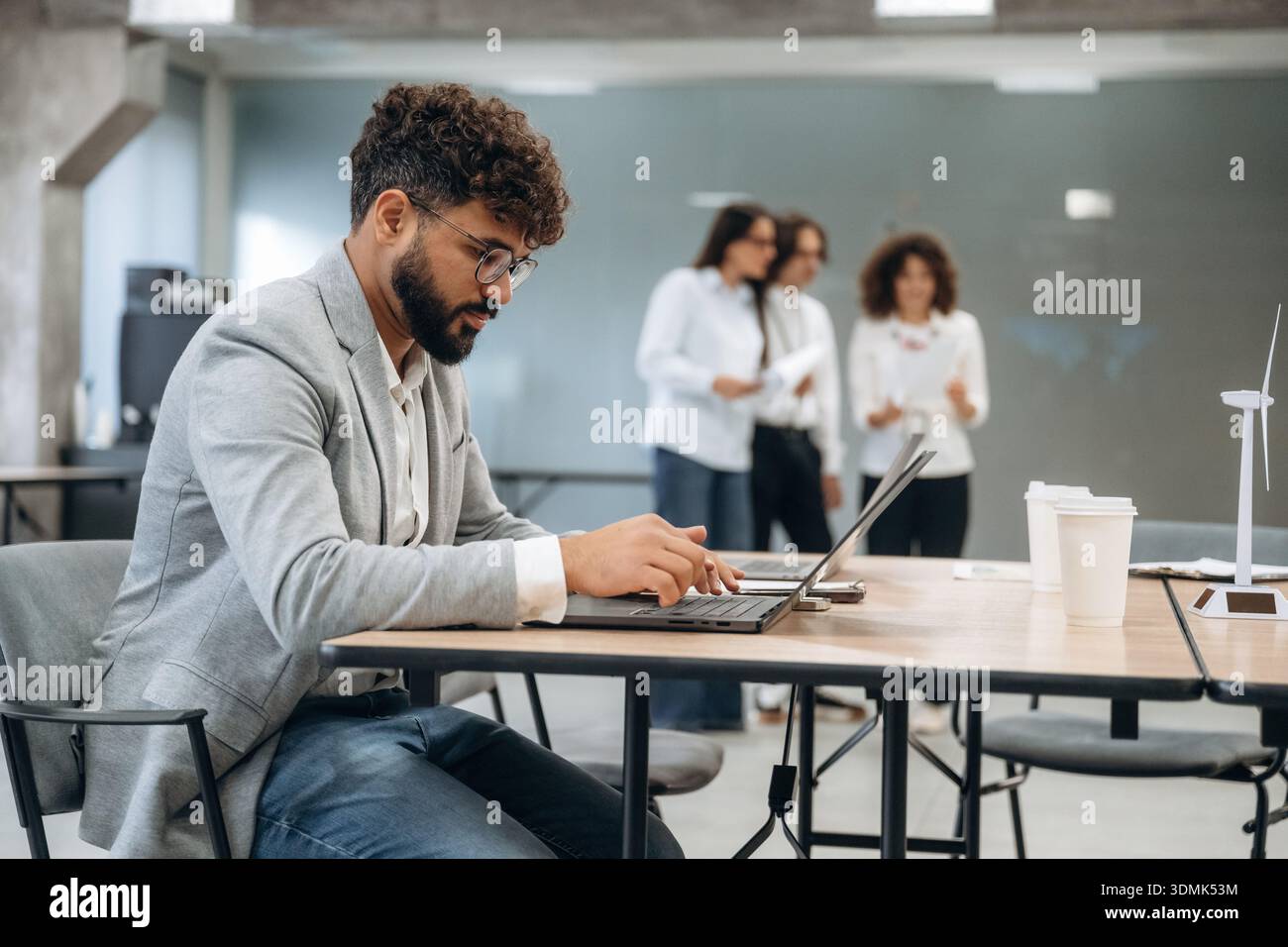 L'uomo con gli occhiali è seduto sulla sedia. Un gruppo di persone lavora in ufficio insieme come un team. Foto Stock