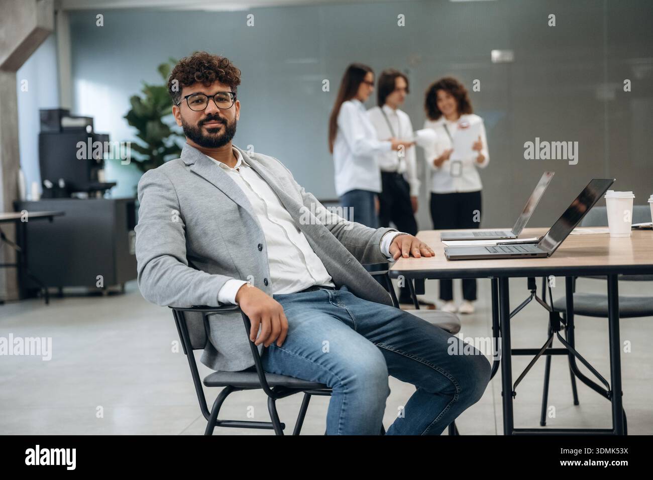 L'uomo con gli occhiali è seduto sulla sedia. Un gruppo di persone lavora in ufficio insieme come un team. Foto Stock