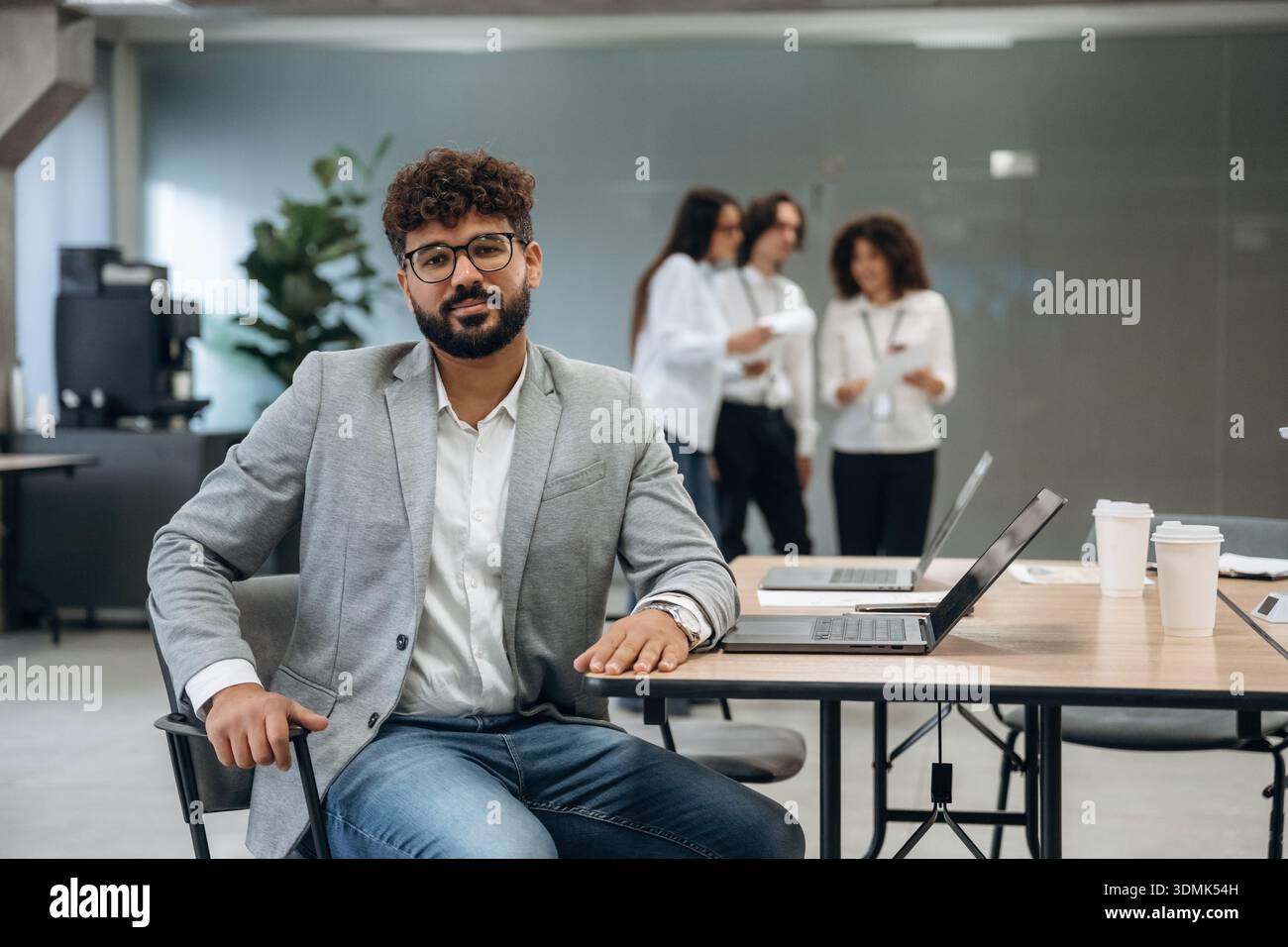 L'uomo con gli occhiali è seduto sulla sedia. Un gruppo di persone lavora in ufficio insieme come un team. Foto Stock