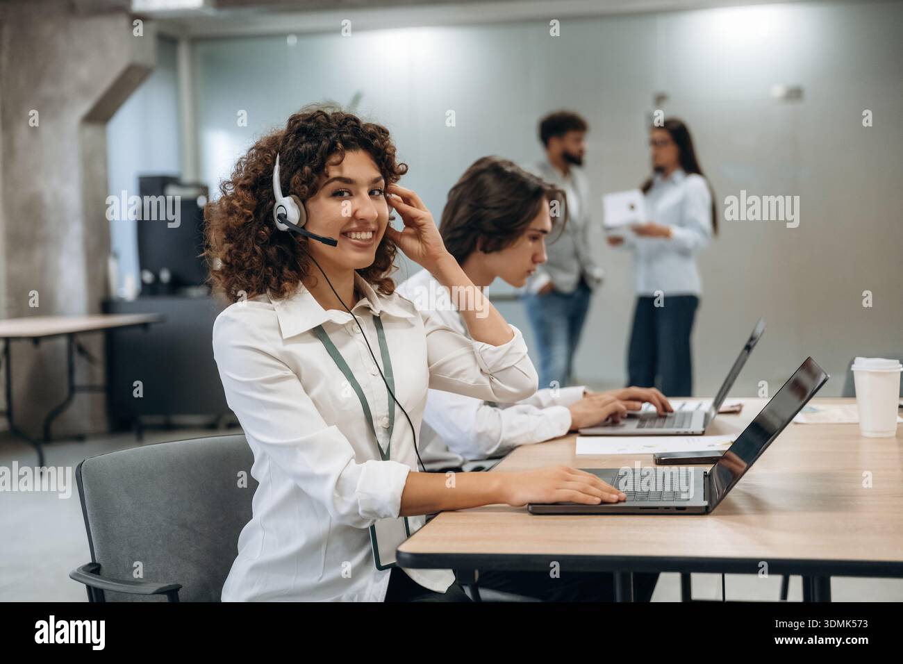 Call Center, donna con le cuffie. Un gruppo di persone lavora in ufficio insieme come un team. Foto Stock