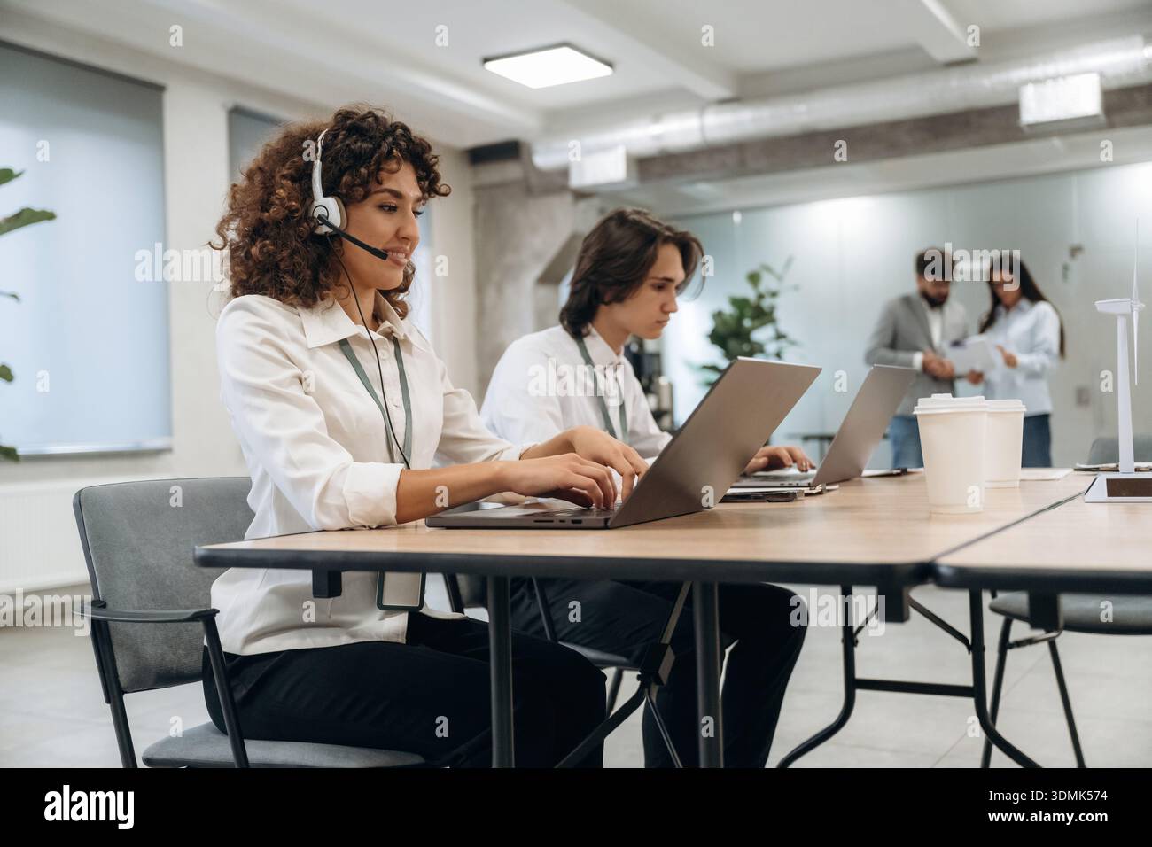 Call Center, donna con le cuffie. Un gruppo di persone lavora in ufficio insieme come un team. Foto Stock