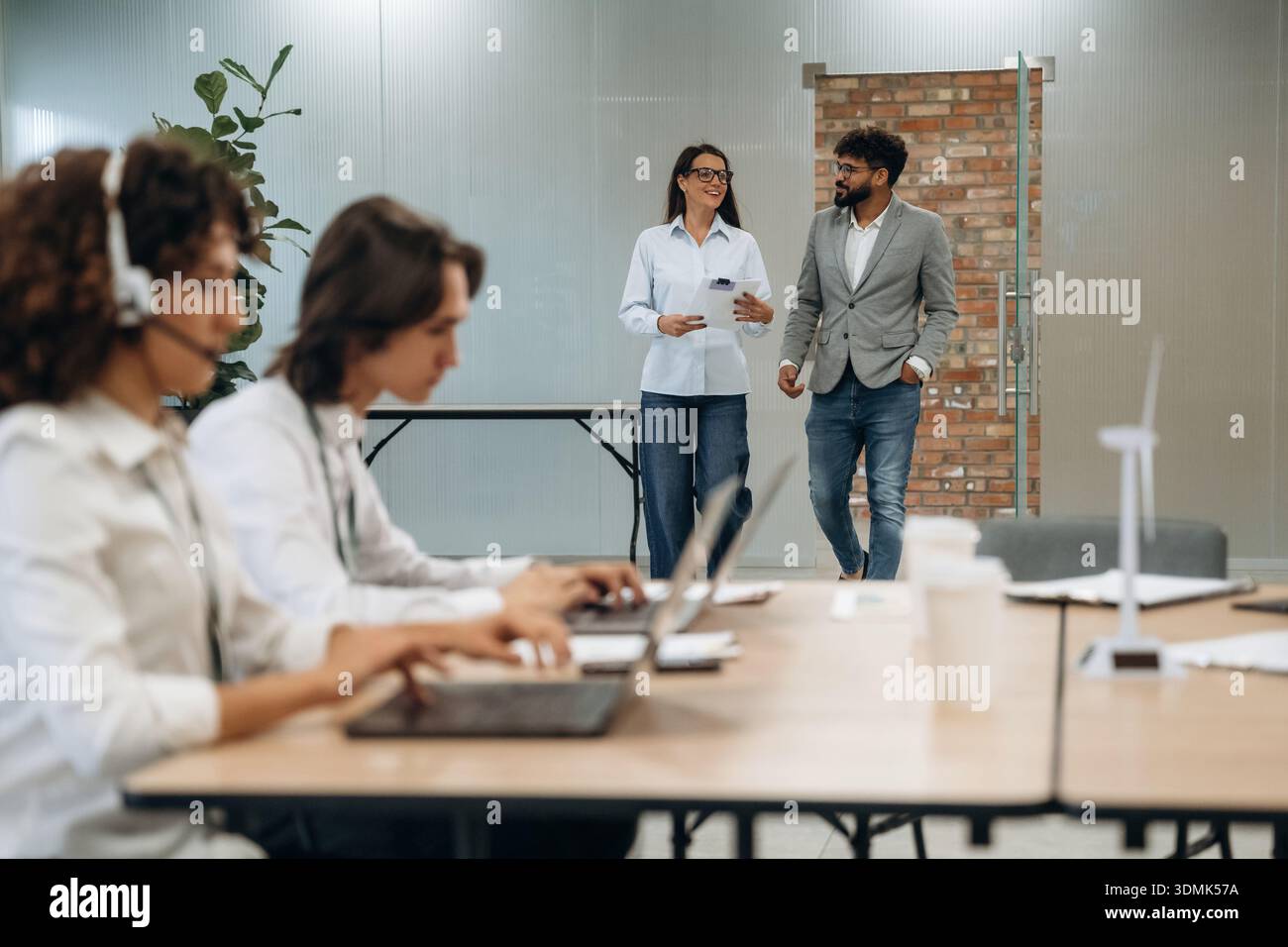 Call Center, donna con le cuffie. Un gruppo di persone lavora in ufficio insieme come un team. Foto Stock