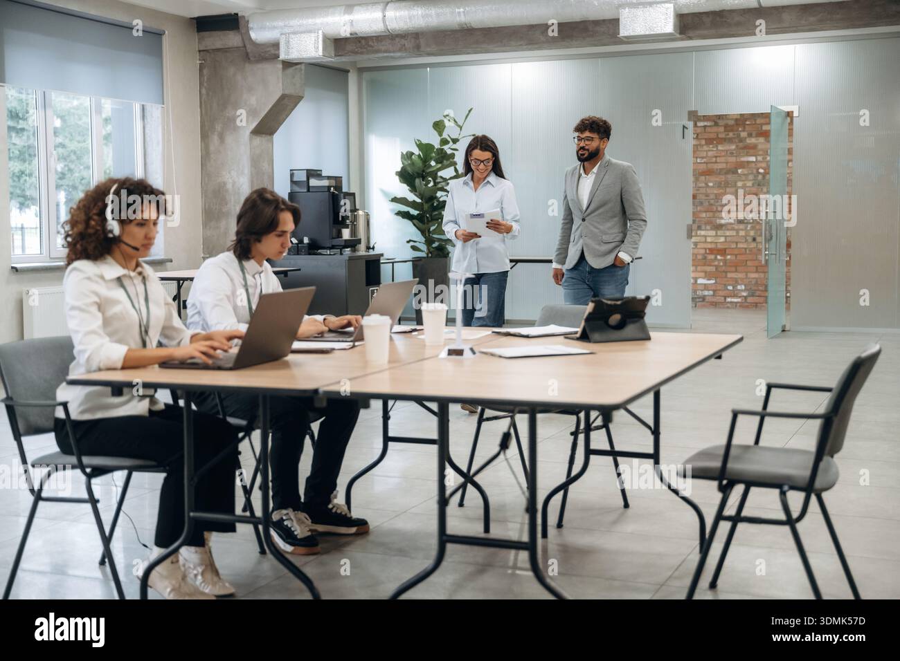 Call Center, donna con le cuffie. Un gruppo di persone lavora in ufficio insieme come un team. Foto Stock