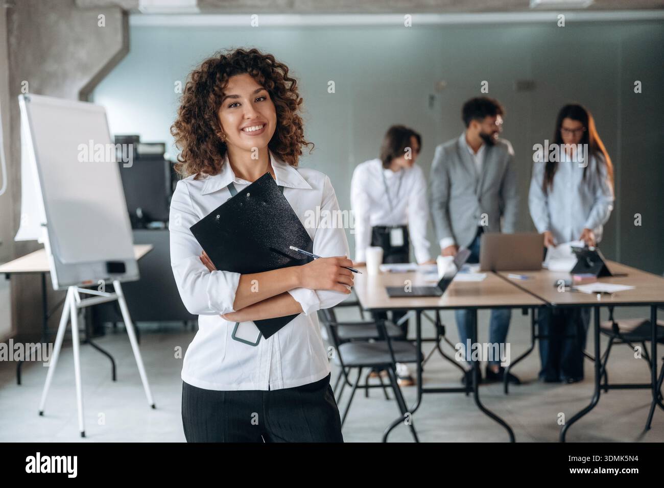 La donna è in piedi e ha un blocco note. Un gruppo di persone lavora in ufficio insieme come un team. Foto Stock