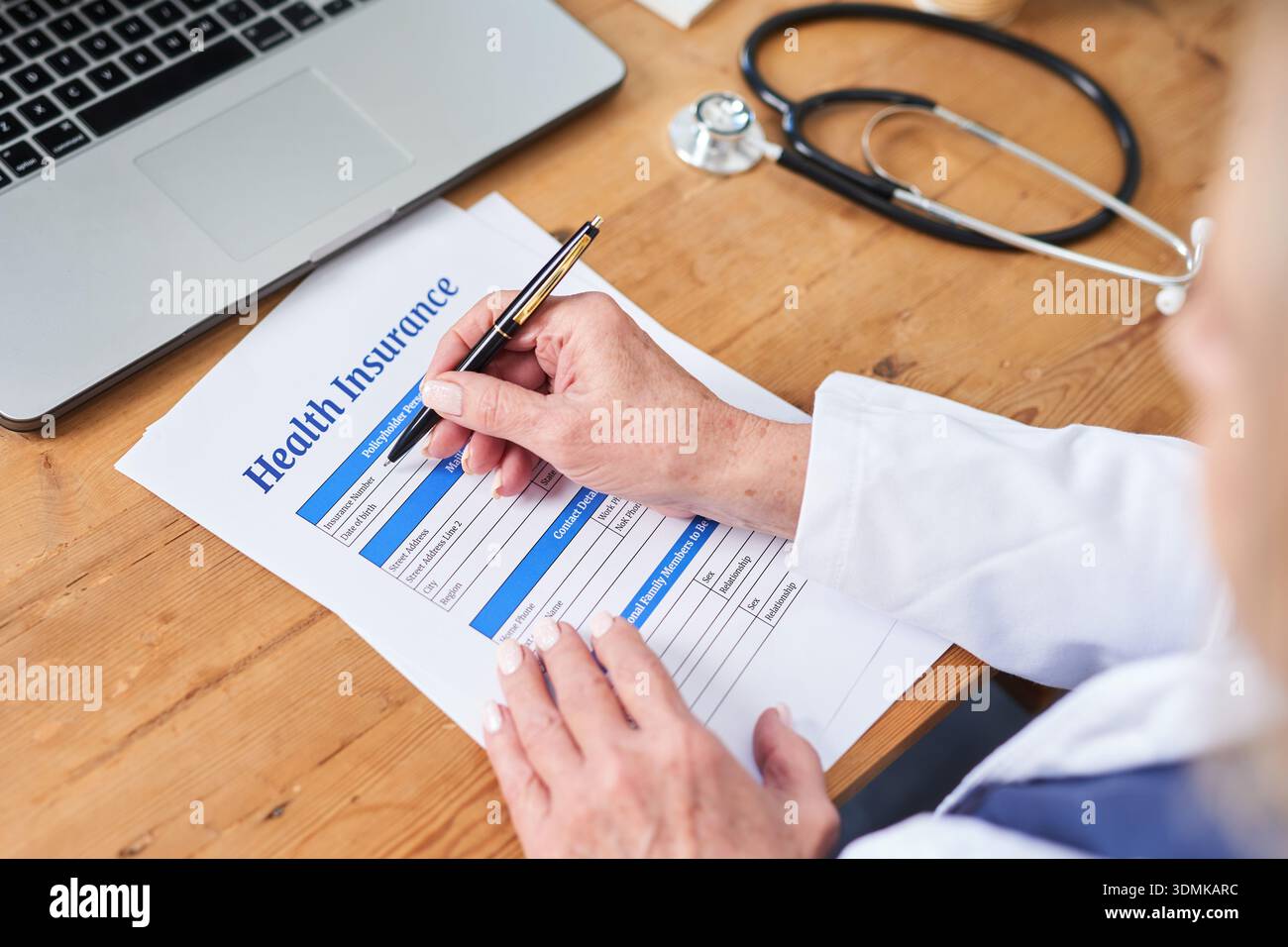 Modulo di assicurazione sanitaria in fase di completamento da parte del medico alla scrivania con laptop e stetoscopio Foto Stock