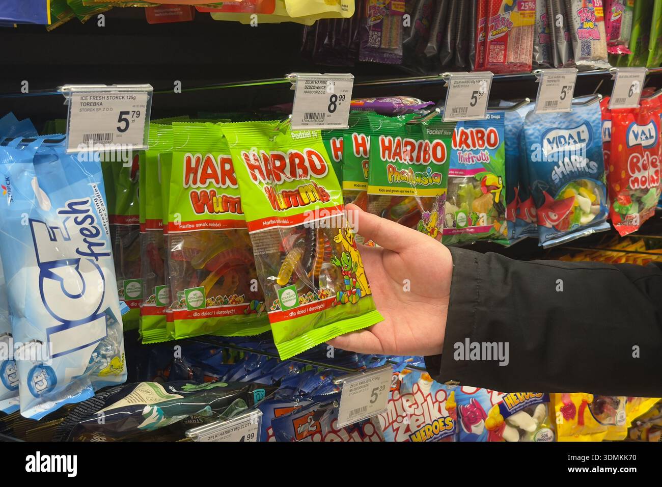 Poznan, Polonia - 22 novembre 2025: La mano arriva per una borsa di caramelle gommose Haribo su uno scaffale affollato del supermercato, mostrando la selezione quotidiana dei consumatori Foto Stock