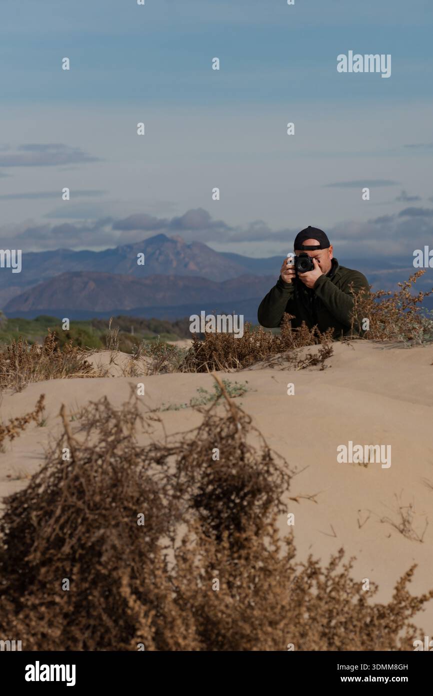 Fotografo che scatta una foto di un paesaggio costiero con dune di sabbia e montagne in lontananza Foto Stock