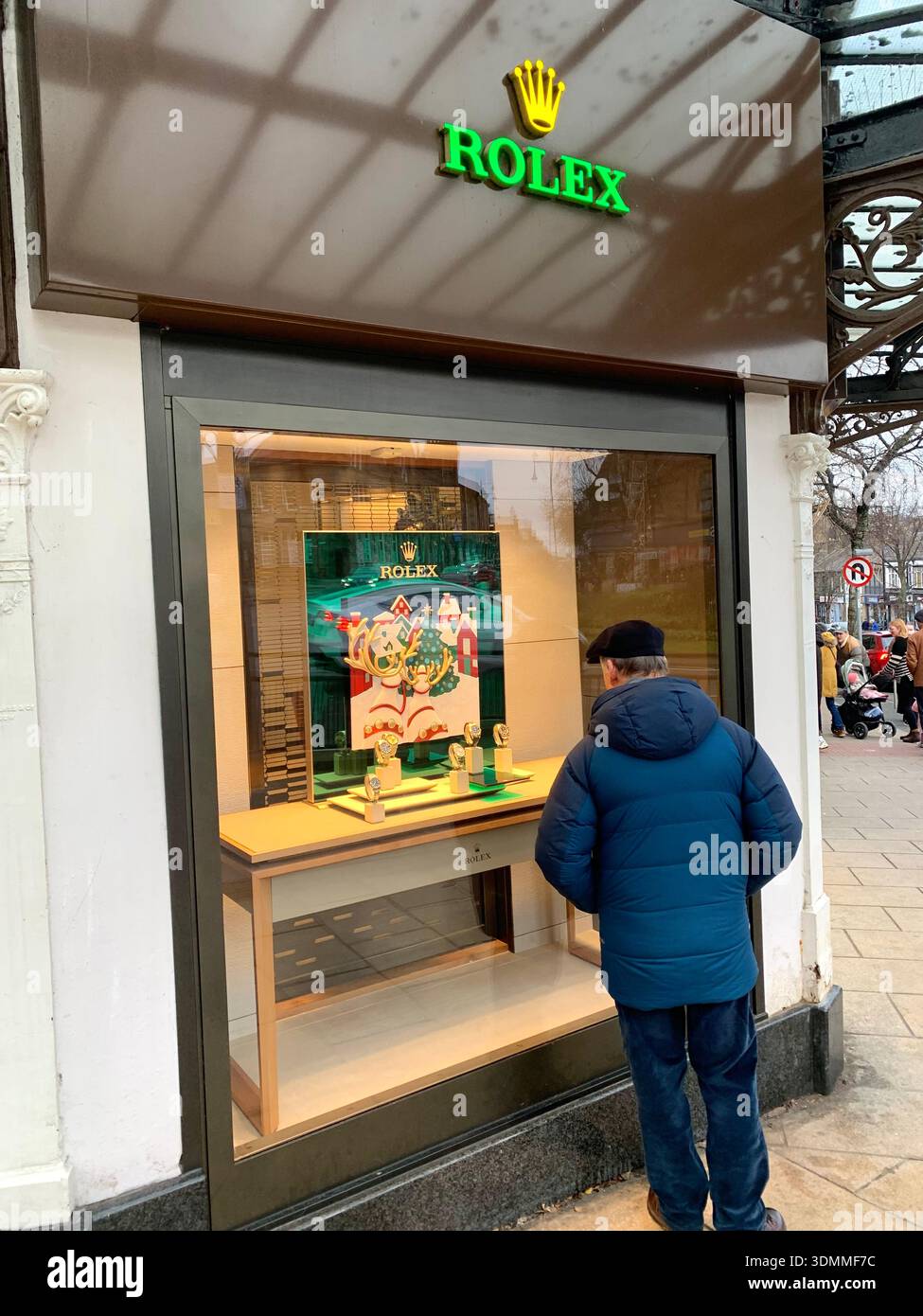 Un passante fa una pausa per guardare gli orologi Rolex in una vetrina su una strada della città con un poster promozionale natalizio e un orologio di lusso in mostra - Immagine stock catturata con smartphone