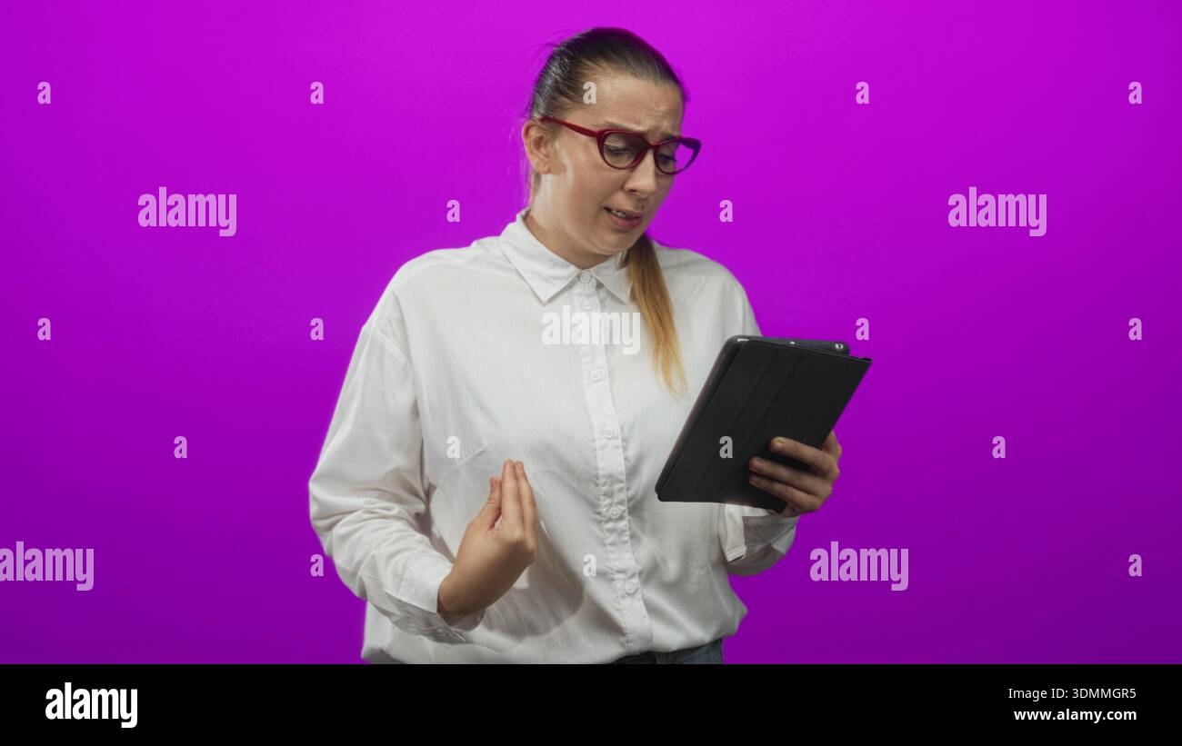 Donna che tiene un tablet, sgombra e gesta con la mano mentre legge lo schermo in uno studio; frustrazione confusione. Foto Stock