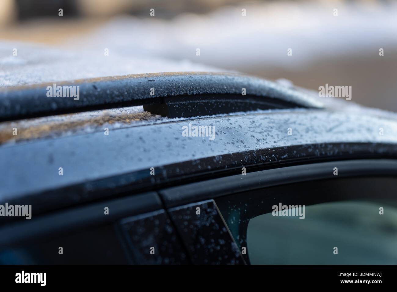 Primo piano invernale del tetto del veicolo e del bordo del finestrino laterale con barra del tetto, sottile strato di ghiaccio e cordoni di ghiaccio che fondono, texture astratta per auto in morbido bokeh Foto Stock
