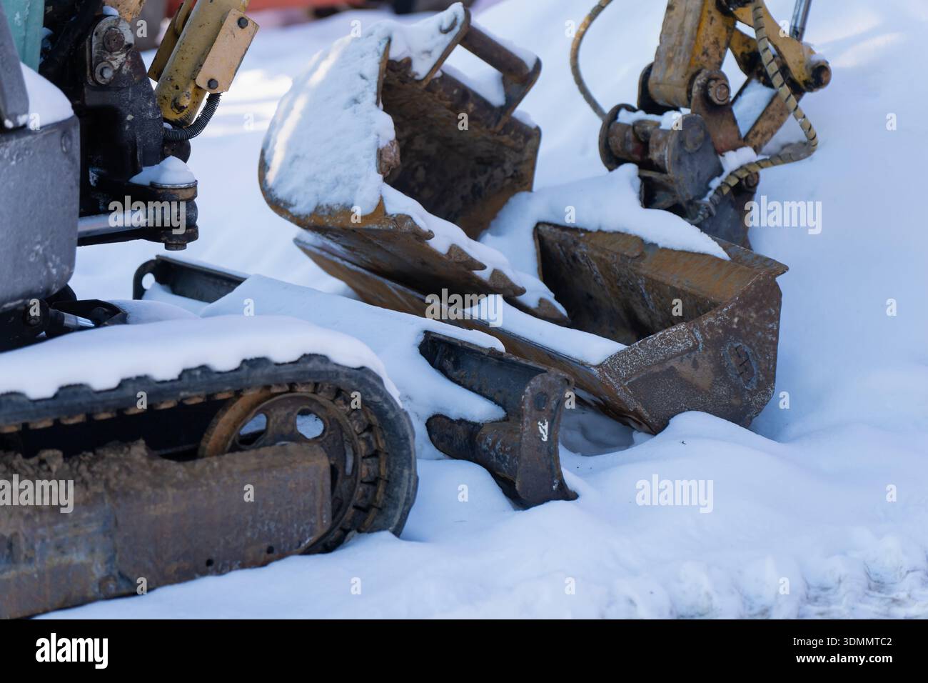 Attrezzature per escavatore innevate con superfici in acciaio usurate, giunti idraulici e dettagli del carro cingolato, macchinari pesanti parcheggiati all'aperto Foto Stock