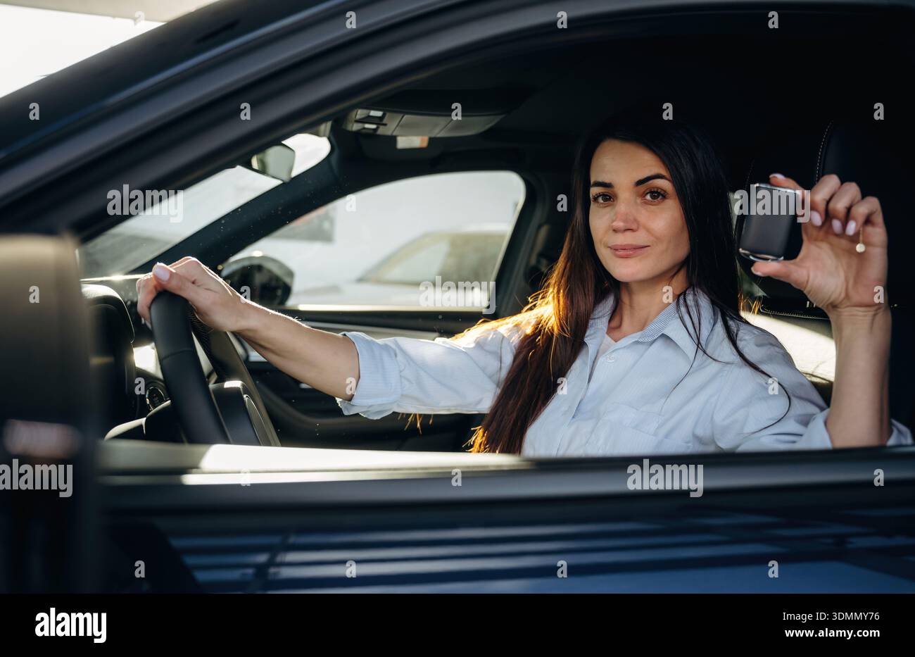 L'orgoglioso proprietario tiene le chiavi. La donna è seduta nell'auto moderna, felice nuovo proprietario. Foto Stock
