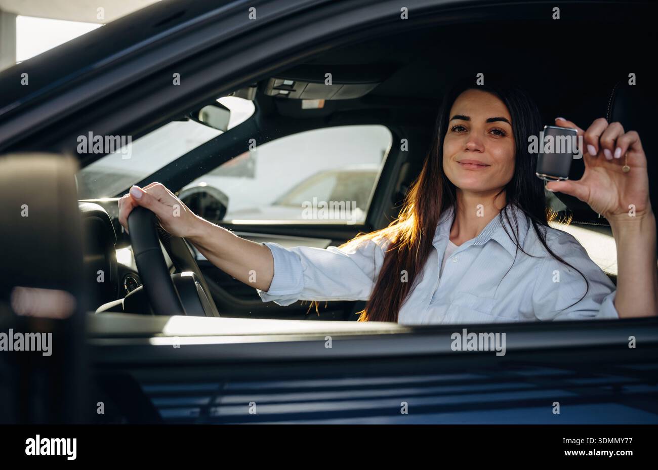 L'orgoglioso proprietario tiene le chiavi. La donna è seduta nell'auto moderna, felice nuovo proprietario. Foto Stock