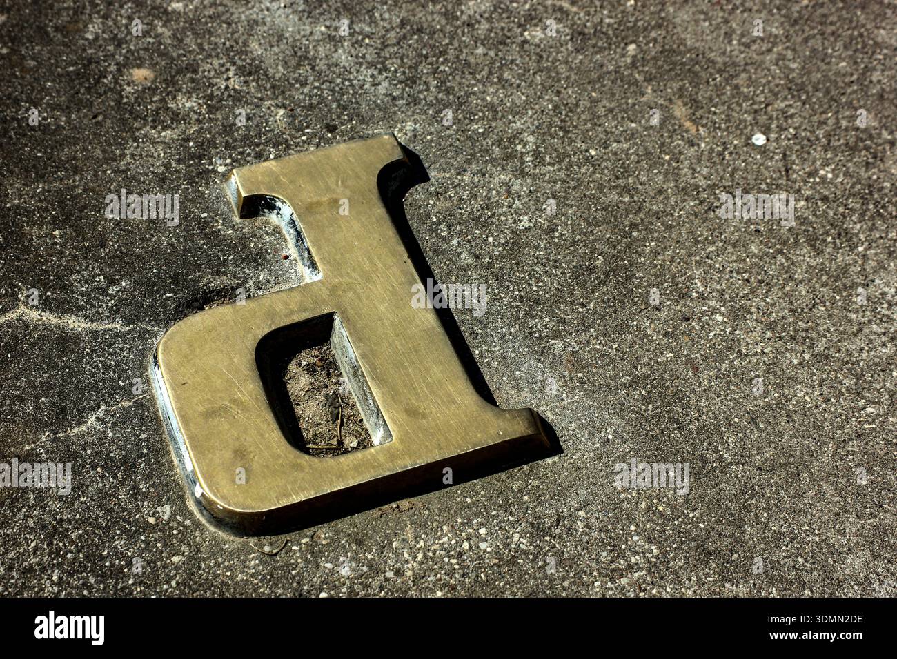 Ottone intemprato minuscola "d" incastonata in calcestruzzo Foto Stock