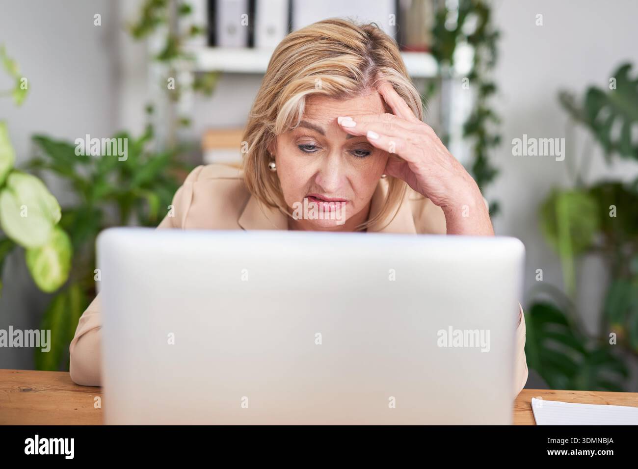 Donna professionista alla scrivania che guarda stressata mentre lavora su un notebook in Bright Office Foto Stock