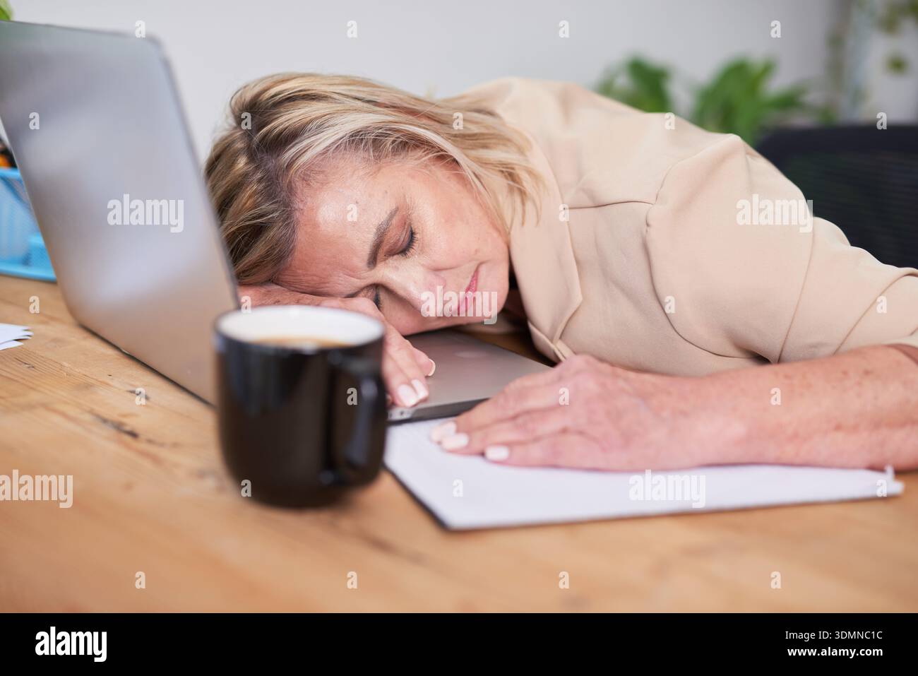 Stanco professionista dorme alla scrivania con laptop e caffè in ufficio Foto Stock