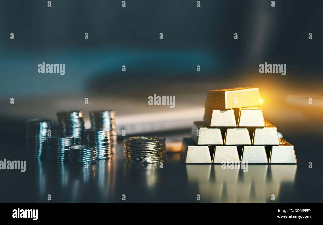 Pila di barre d'oro e pile di monete d'argento sulla scrivania scura dell'ufficio. Concetto di gestione patrimoniale, investimento sicuro, stabilità finanziaria e capite Foto Stock