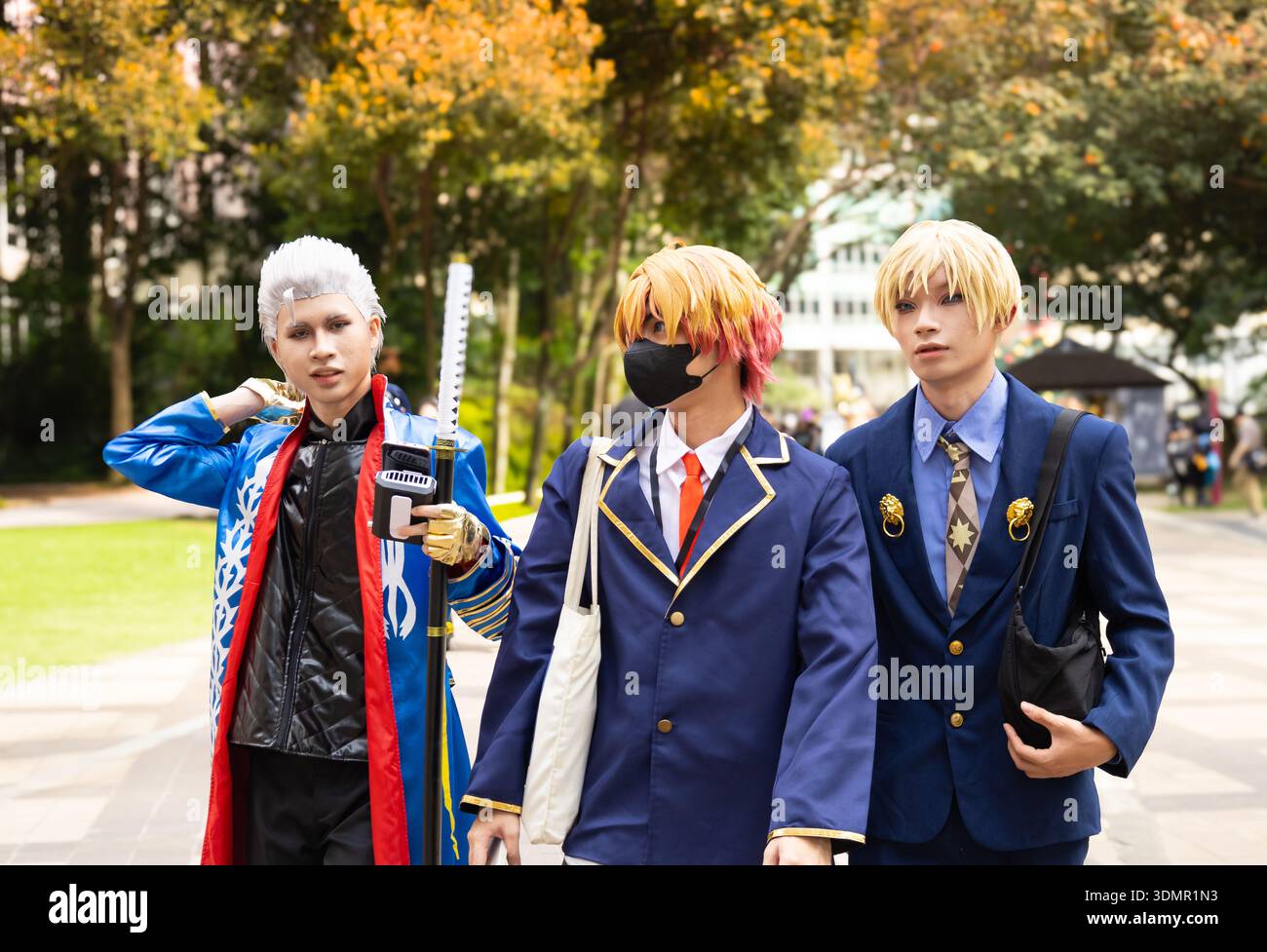 Gruppo di tre cosplayer che ritraggono personaggi di Ensemble Stars! in divise scolastiche dettagliate e abiti da idolo in una convention di anime all'aperto. Foto Stock