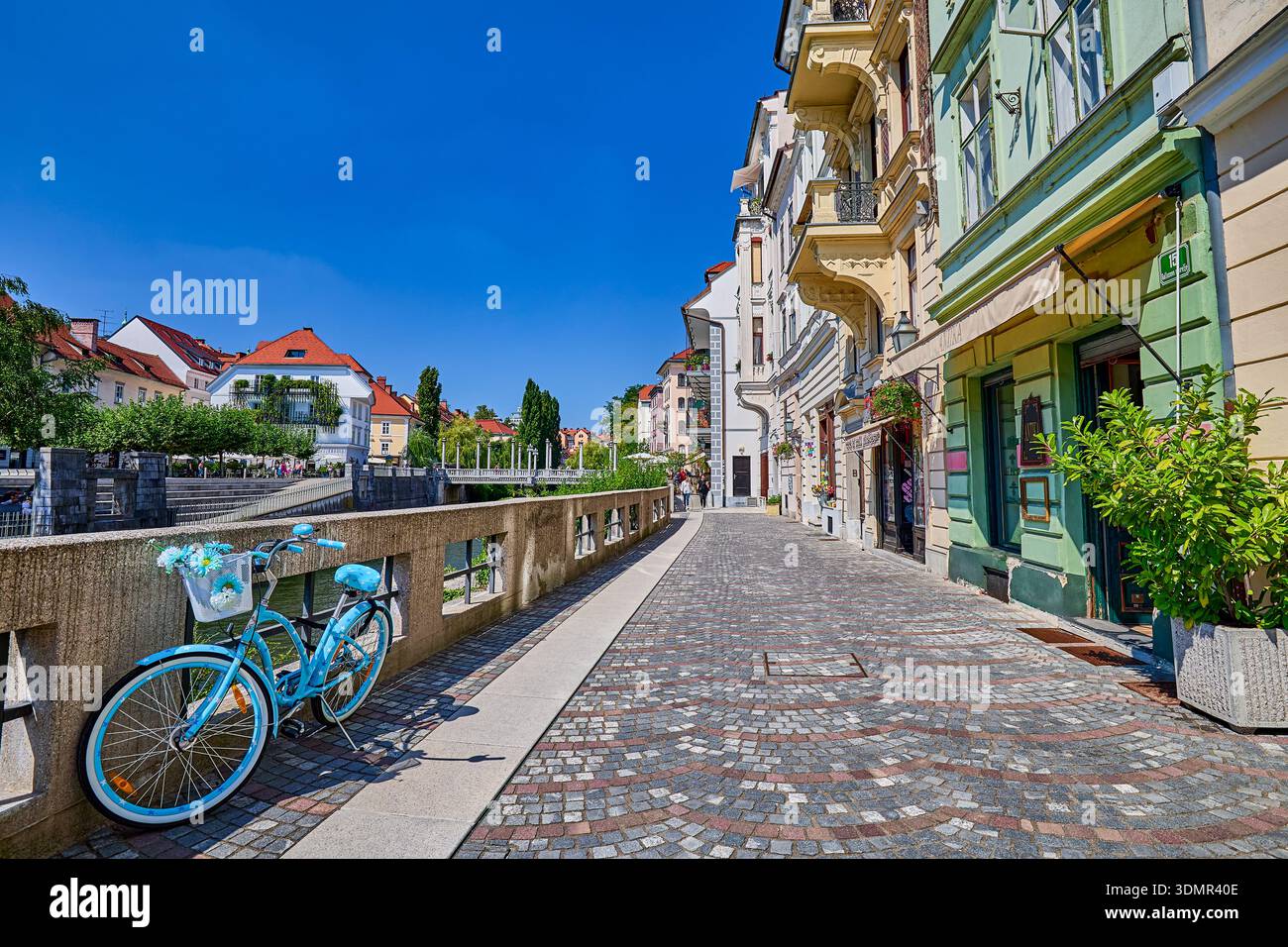 Negozi al dettaglio in strada acciottolata presso il Breg Embankment del fiume Lubiana con una bicicletta colorata blu, Lubiana, Slovenia centrale, Europa Foto Stock