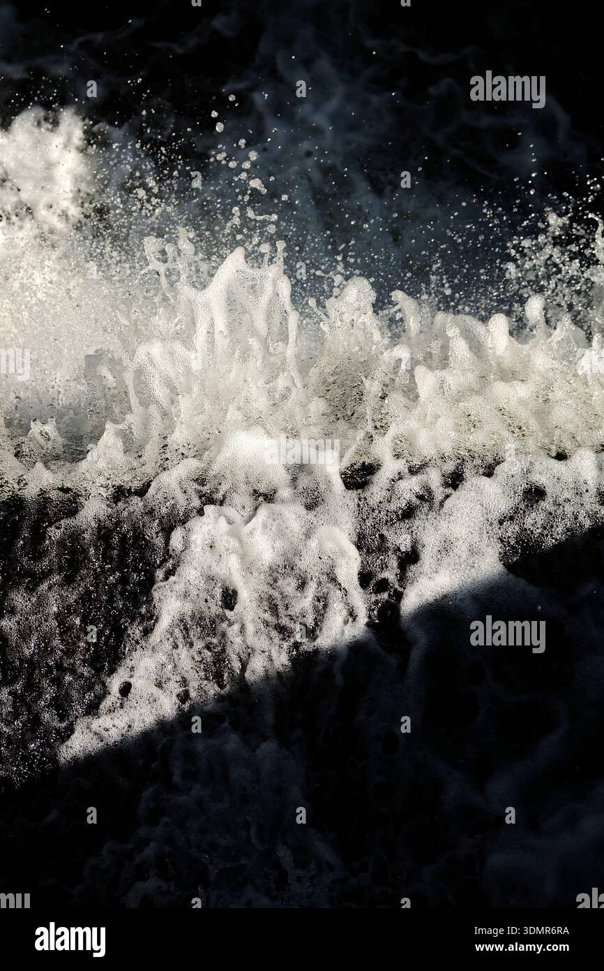 Primo piano di acque turbolente del fiume che si schiantano e spruzzano, catturati in una luce spettacolare su uno sfondo scuro. Movimento congelato, goccioline volanti e st Foto Stock