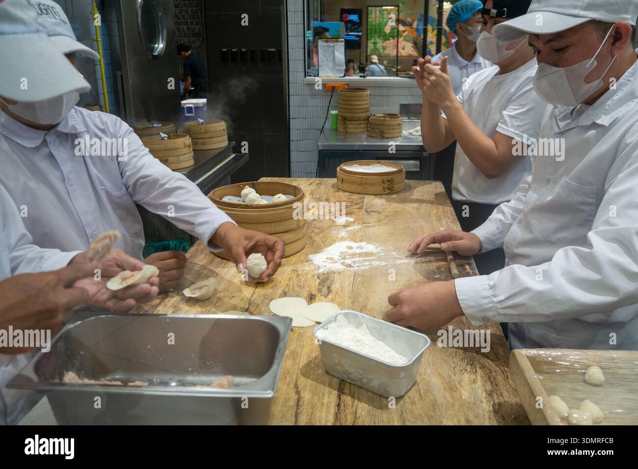 I cuochi del ristorante asiatico preparano a mano panini freschi nikuman al vapore nella cucina a vista dietro il banco di vetro all'interno del moderno centro commerciale outlet di cibo Foto Stock
