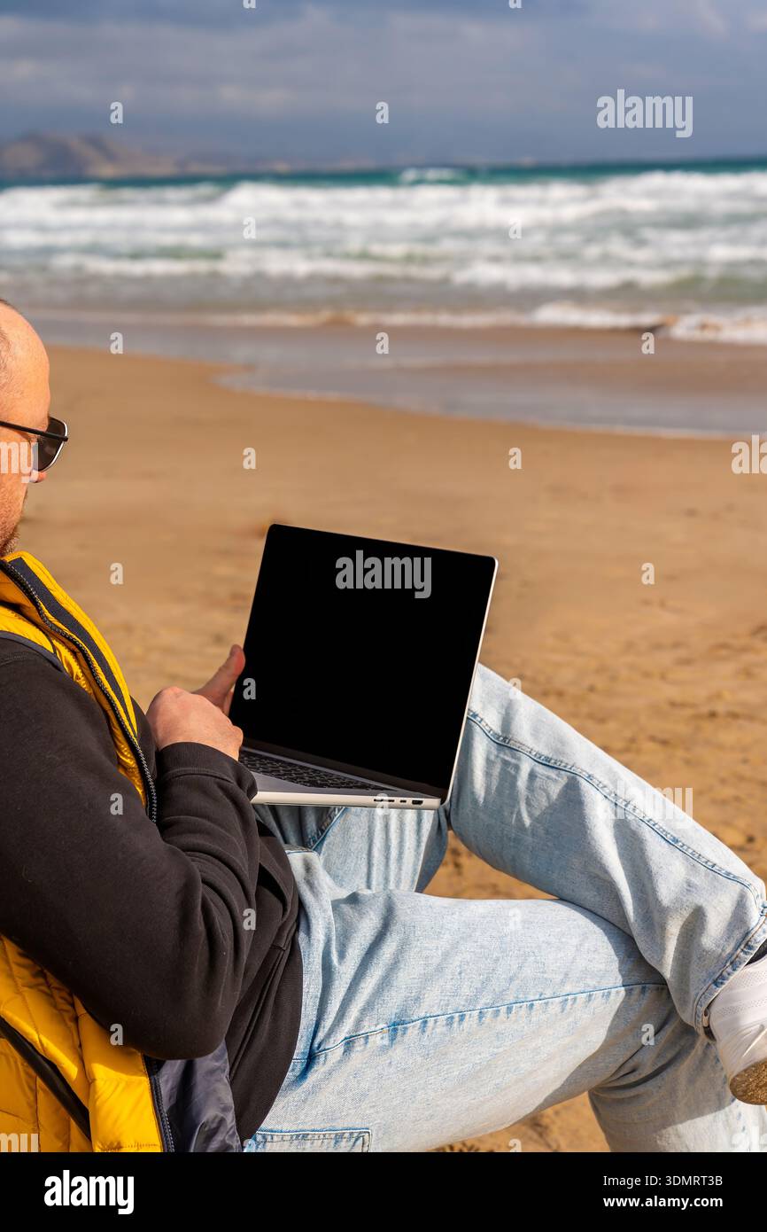 Digitazione individuale su un laptop in mezzo a un tranquillo paesaggio marino. Persona impegnata in attività di codifica su un laptop vicino a onde oceaniche tranquille Foto Stock