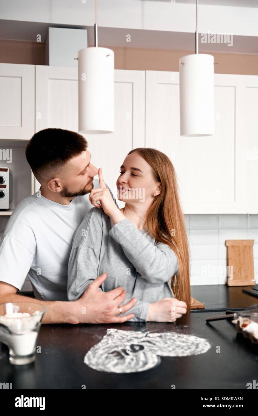 Una coppia sta insieme in una cucina ridendo e toccando scherzosamente i volti mentre preparano un pasto. Sembra che si godano il loro tempo insieme Foto Stock