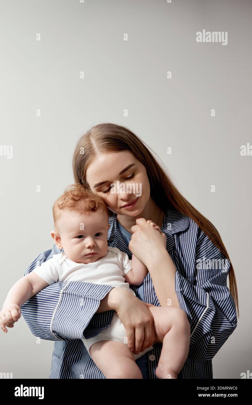 La madre abbraccia il suo bambino carino in un caldo ambiente interno, evidenziando un bellissimo momento d'amore e di connessione tra di loro Foto Stock