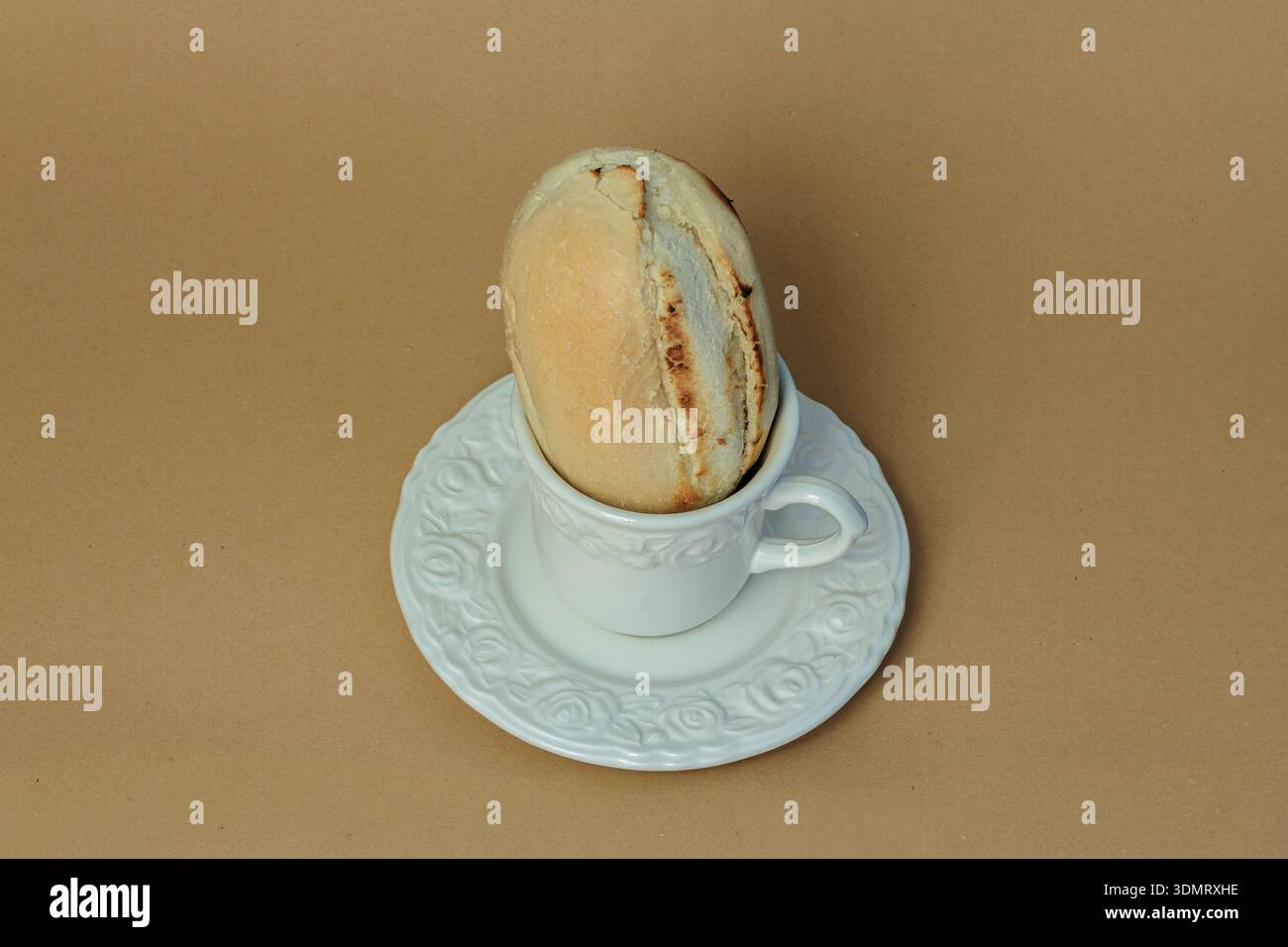 Composizione minimalista surreale con panino inserito in una tazza da caffè bianca. Concetto creativo di arte culinaria sul beige. Foto Stock