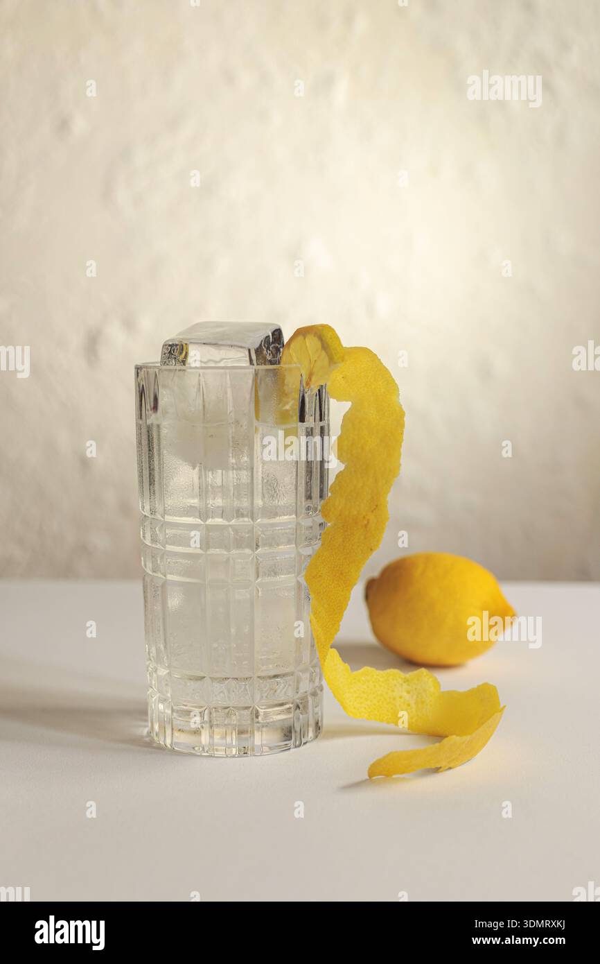 Bicchiere da cocktail con cubetti di ghiaccio grandi e una lunga scorza di limone. Presentazione artistica di un drink. Foto Stock