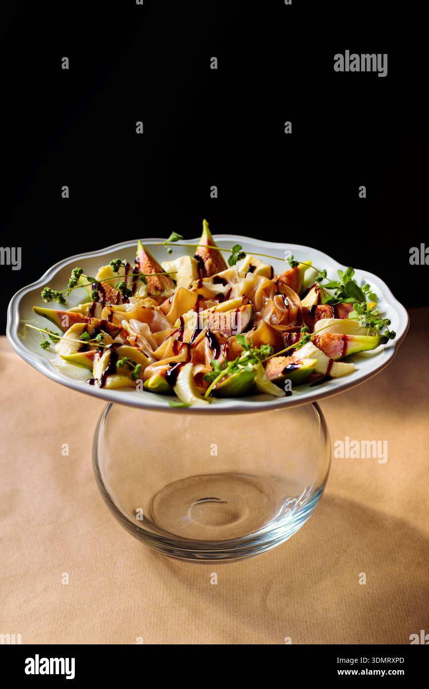 Elegante insalata di fichi con glassa balsamica su supporto di vetro su sfondo nero. Fotografia gastronomica straordinaria. Foto Stock