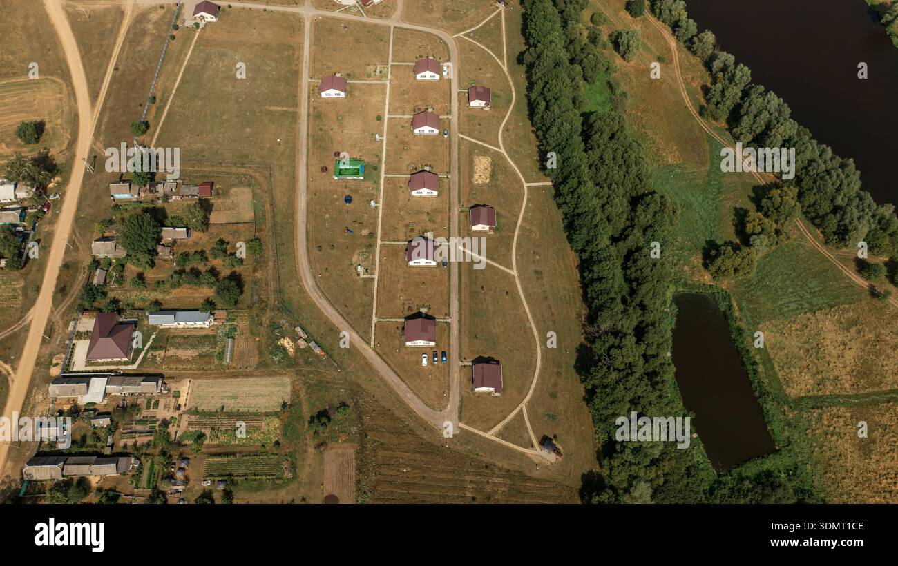 Prospettiva aerea di un piccolo insediamento vicino a Berezivka o Minsk, Bielorussia, con case dal tetto rosso, campi aperti, un fiume, uno stagno e un appezzamento agricolo Foto Stock