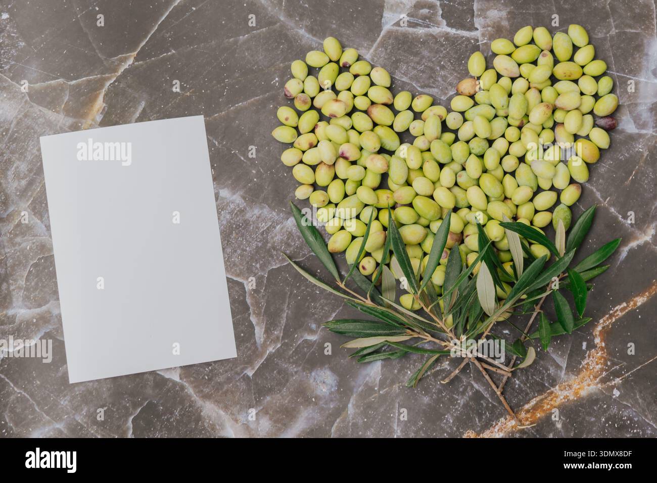 Olive verdi appena raccolte disposte a forma di cuore su superficie di marmo, ricche vitamine del superfood mediterraneo con carta bianca per lo spazio delle copie Foto Stock