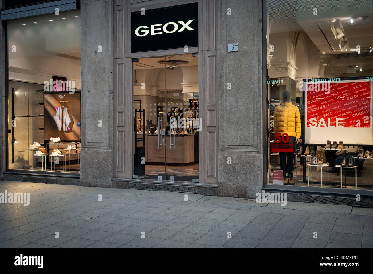 Milano, Italia - 2026, 3 Feb: Vetrina Geox FW25 con eleganti espositori di scarpe, design moderno e vivaci cartellonistica di vendita, che catturano l'essenza della Foto Stock