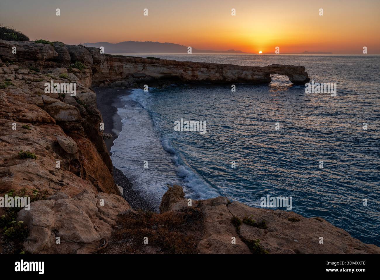 Arco marino in pietra calcarea naturale a Skaleta sull'isola di Creta, Grecia, catturato durante la calda luce del tramonto sopra il Mar Mediterraneo con onde calme e drammi Foto Stock