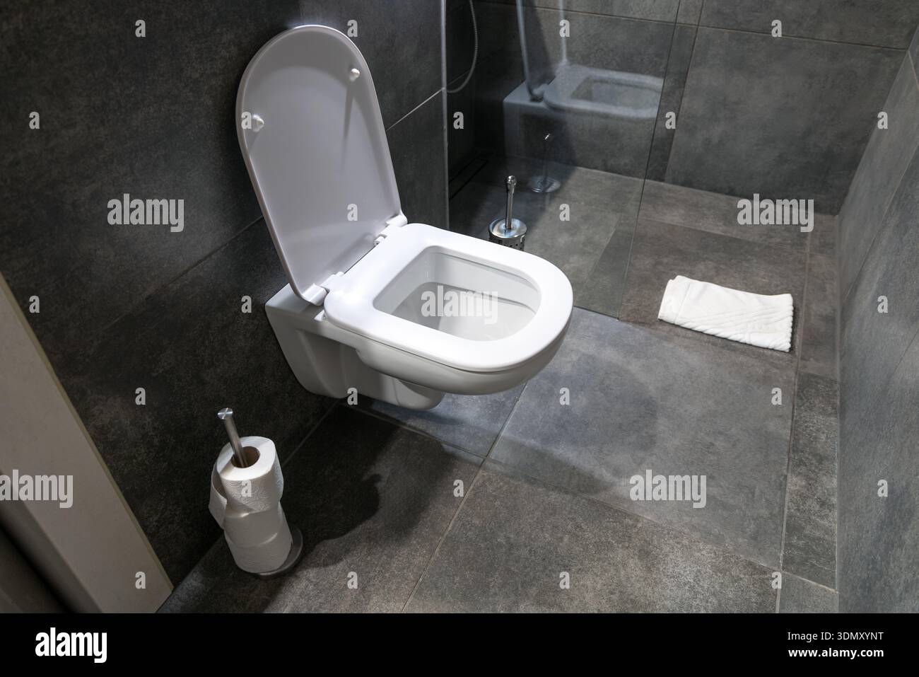 WC moderno a parete con coperchio aperto in un bagno combinato con piastrelle in ceramica grigio scuro, doccia in vetro e tappetino bianco, che mostra un design igienico pulito e interni moderni Foto Stock