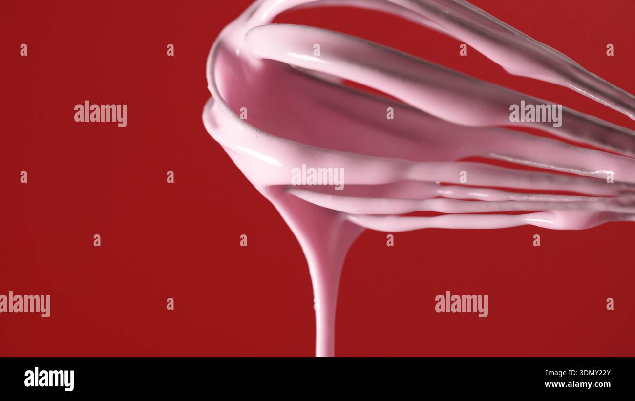 Montare l'impasto rosa in un recipiente su sfondo rosso durante una sessione di cottura in cucina Foto Stock
